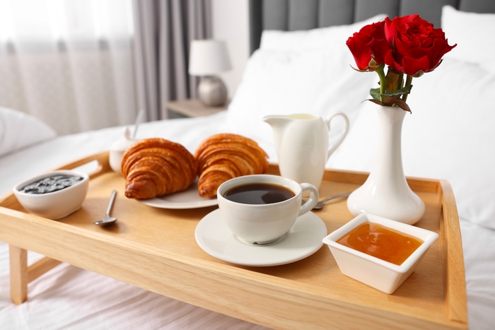 uma bandeja com café, dois croassant, e um vaso de flores.