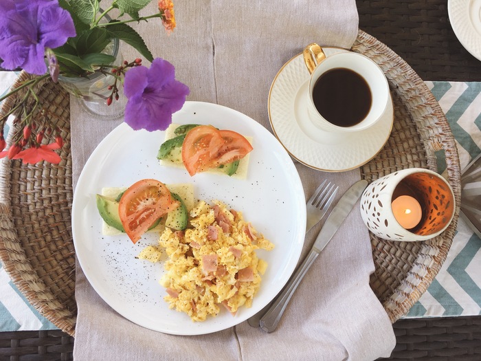 uma bandeja de café, com um prato com ovo mexido, queijo, tomate e abacate. 