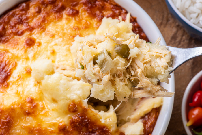 Escondidinho de frango cremoso com purê de batatas e queijo gratinado, servido em uma travessa, com uma porção sendo retirada com um garfo.