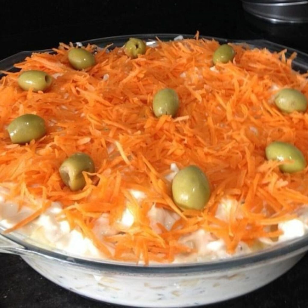 Salada de maionese com cenoura ralada e azeitonas verdes, servida em uma travessa de vidro.