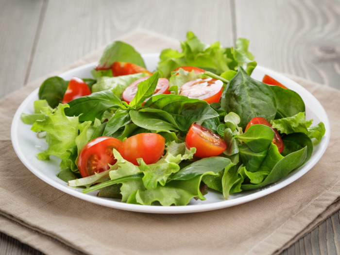 Salada fresca de folhas verdes, espinafre e tomate-cereja cortado ao meio, servida em um prato branco sobre um guardanapo bege.