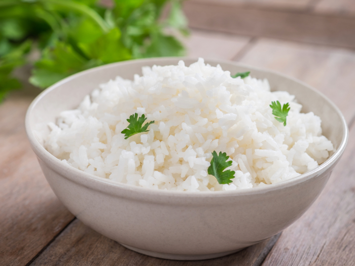 Tigela de arroz branco cozido, decorado com folhas de salsa, servida sobre uma mesa de madeira.