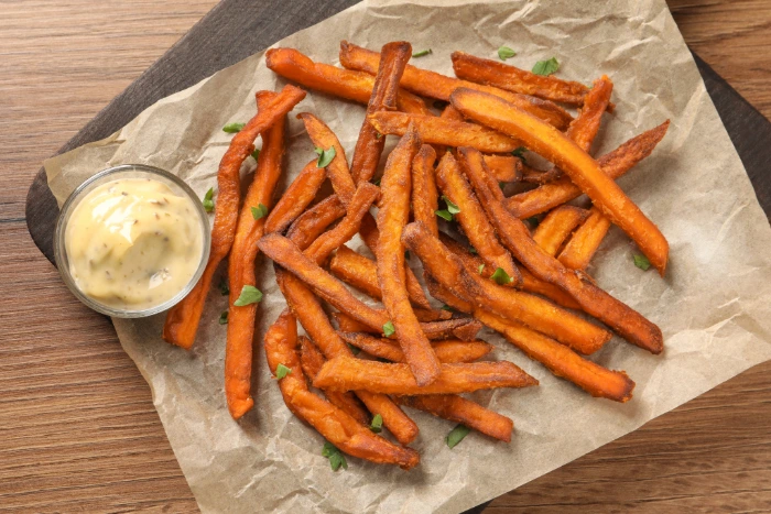 Batata-doce assada servida sobre papel manteiga com molho cremoso de alho em recipiente de vidro