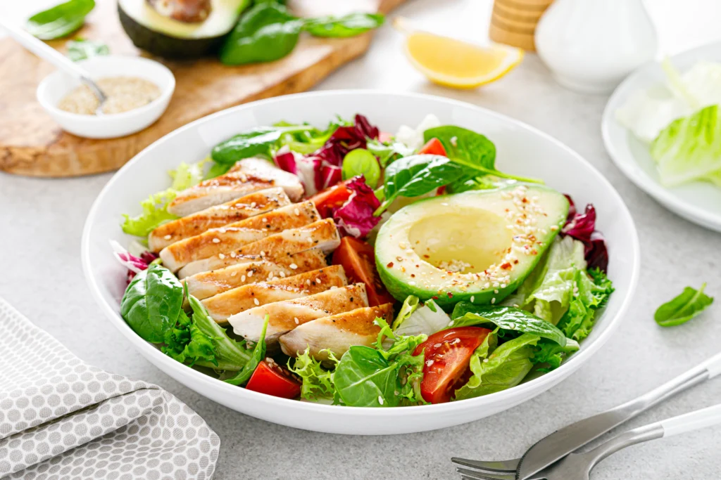Salada nutritiva com frango grelhado fatiado, meio abacate, tomate e folhas verdes em prato branco