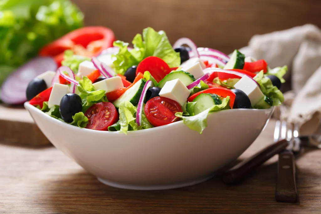Salada grega com alface, tomate-cereja, pepino, azeitonas pretas, queijo branco em cubos e cebola roxa em tigela branca