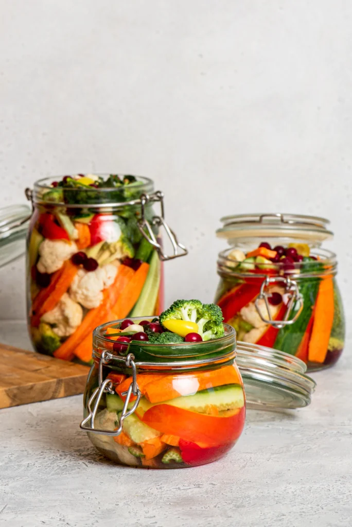 Potes de vidro com saladas coloridas em camadas, contendo brócolis, cenoura, couve-flor, pepino e frutas vermelhas