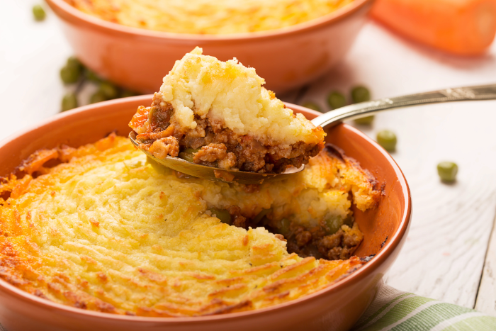 Escondidinho de carne moída com purê de batata dourado sendo servido com colher em travessa de cerâmica, com recheio visível de carne refogada.
