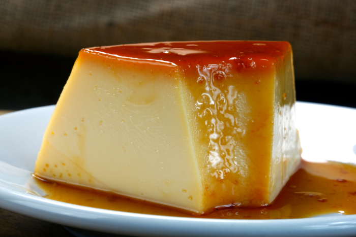 Fatia de pudim de leite condensado com calda dourada em prato branco.
