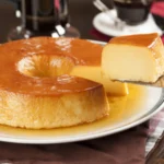 Pudim de leite condensado inteiro com calda e uma fatia sendo servida.