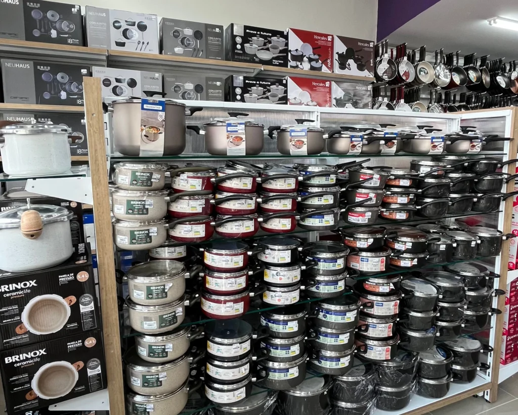 Expositor de panelas e utensílios de cozinha em loja de utilidades domésticas com diferentes modelos de panelas, frigideiras e conjuntos organizados em prateleiras.