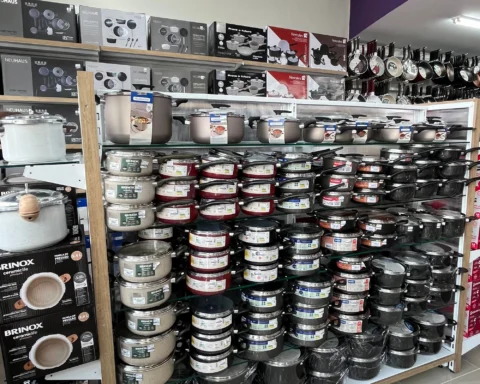 Expositor de panelas e utensílios de cozinha em loja de utilidades domésticas com diferentes modelos de panelas, frigideiras e conjuntos organizados em prateleiras.