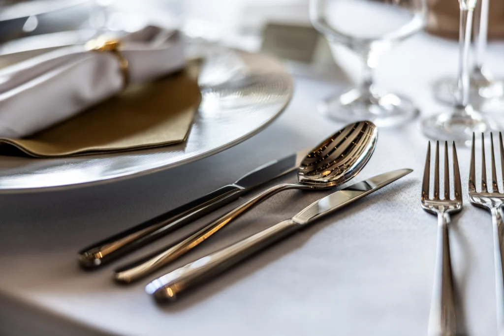 Talheres de mesa em inox com prato e taça sobre mesa posta elegante para refeição.